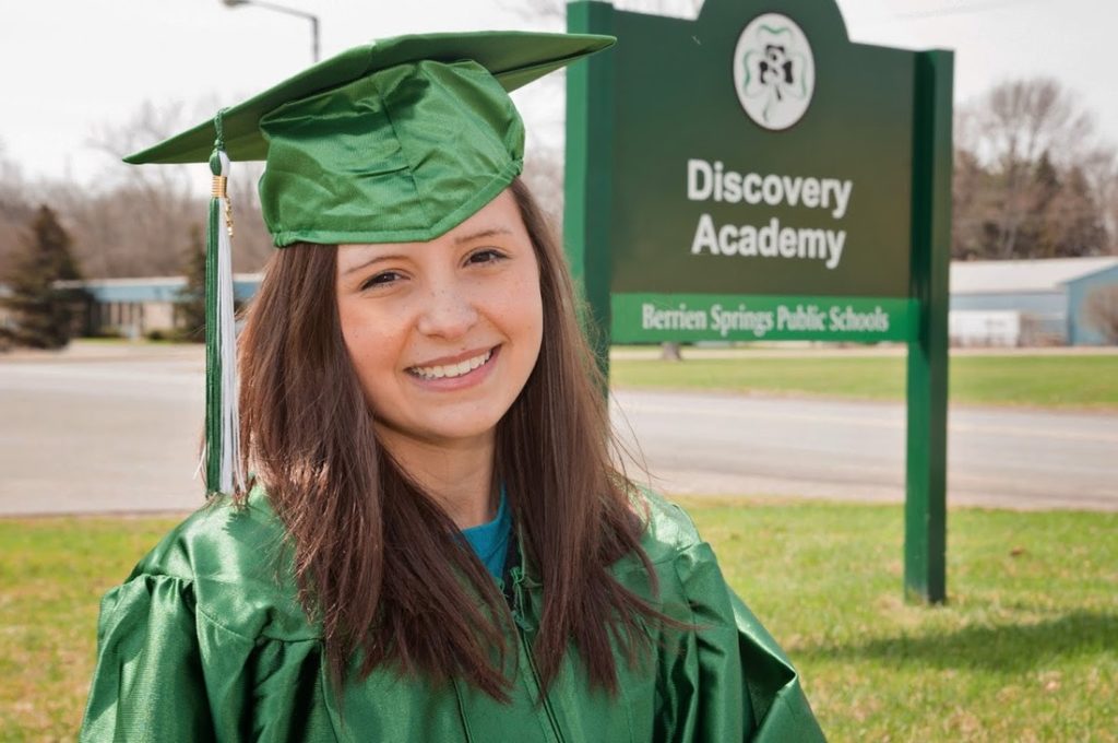 young woman with graduation gown and cap on in from of sign