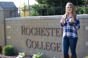 Student with thumbs up in front of Rochester College sign